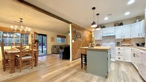 A modern kitchen with wooden flooring, white cabinets, and a central island. - 2 Kings • 2 Queens • Fenced Yard • 2 Firepits! (Lakeside)