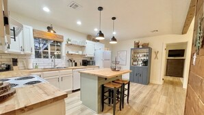 A modern kitchen with a central island, wooden countertops, and bar stools. - 2 Kings • 2 Queens • Fenced Yard • 2 Firepits! (Lakeside)
