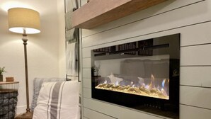 A modern living room with a built-in fireplace, a floor lamp, and a striped cushion on the floor. - 2 Kings • 2 Queens • Fenced Yard • 2 Firepits! (Lakeside)