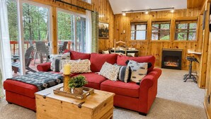 Een gezellig houten interieur met een rode bank, een houten kist en een open haard.