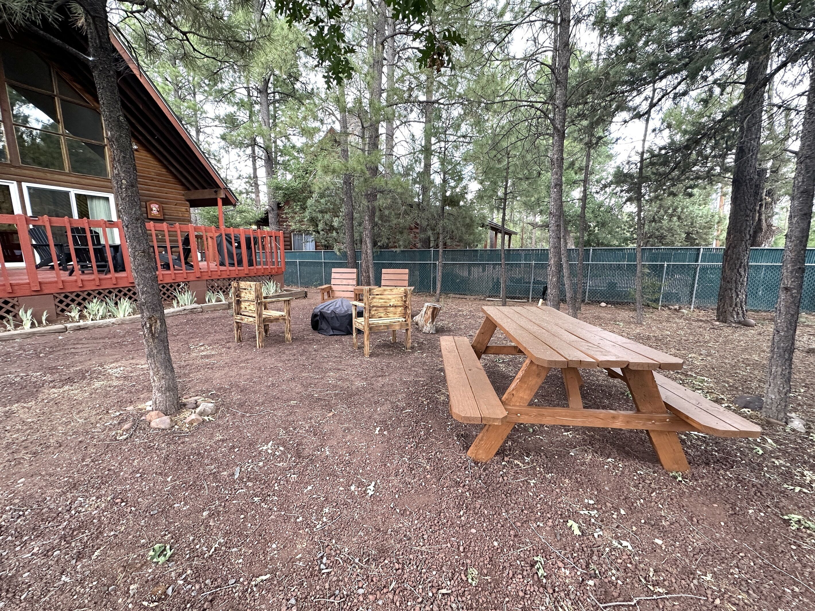 En plats för picknick med ett träbord och bänkar, omgiven av träd och ett inhägnat område.