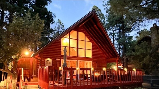 Een houten chalet met een veranda, grote ramen en een goed verlicht interieur.