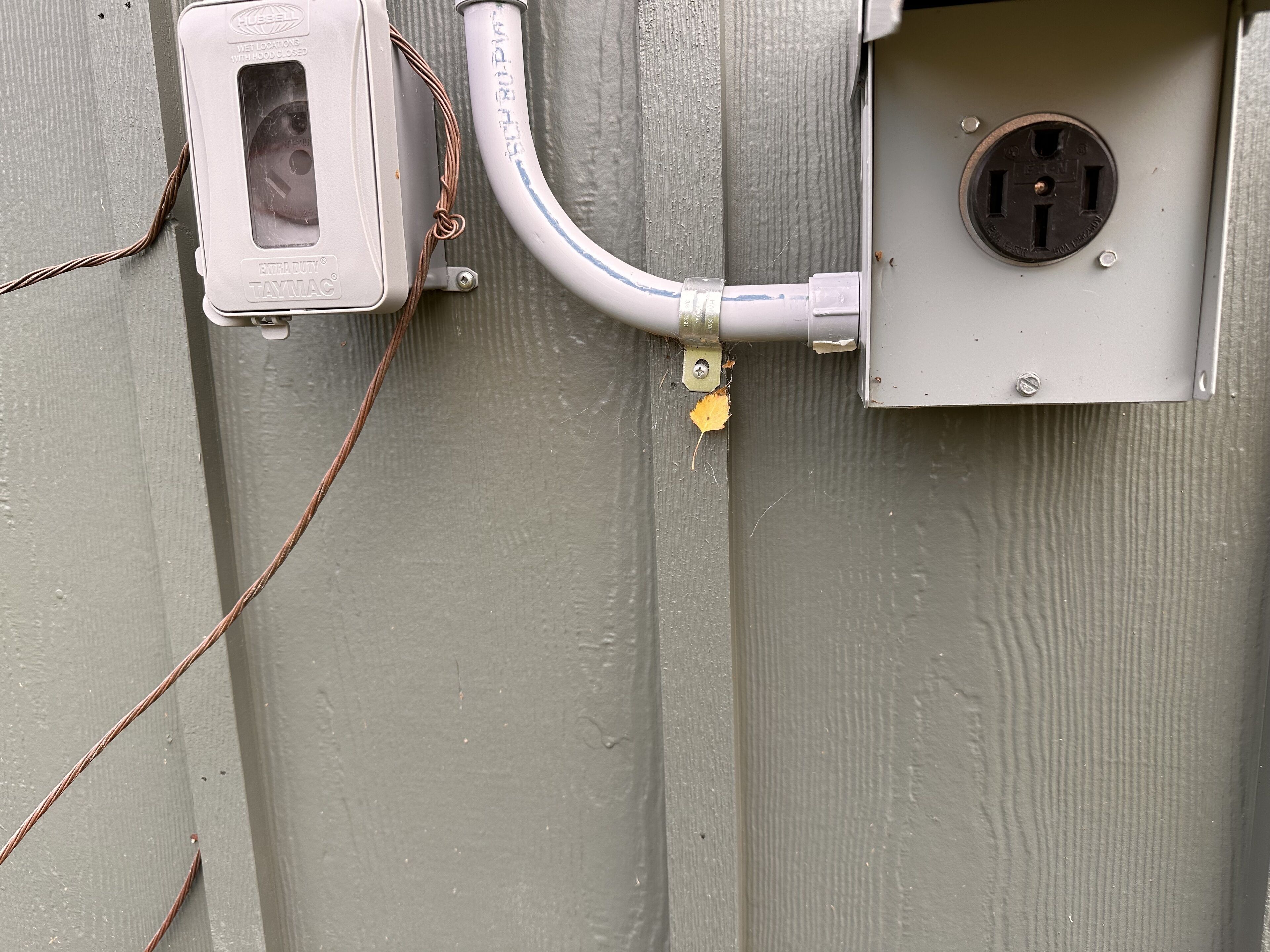 Un cuadro eléctrico con un cable y un candado en una pared gris.