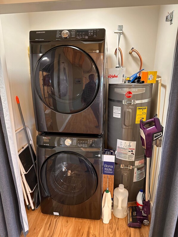 Une buanderie équipée de machines à laver et de sèche-linge superposés, d’un chauffe-eau et de produits de nettoyage.