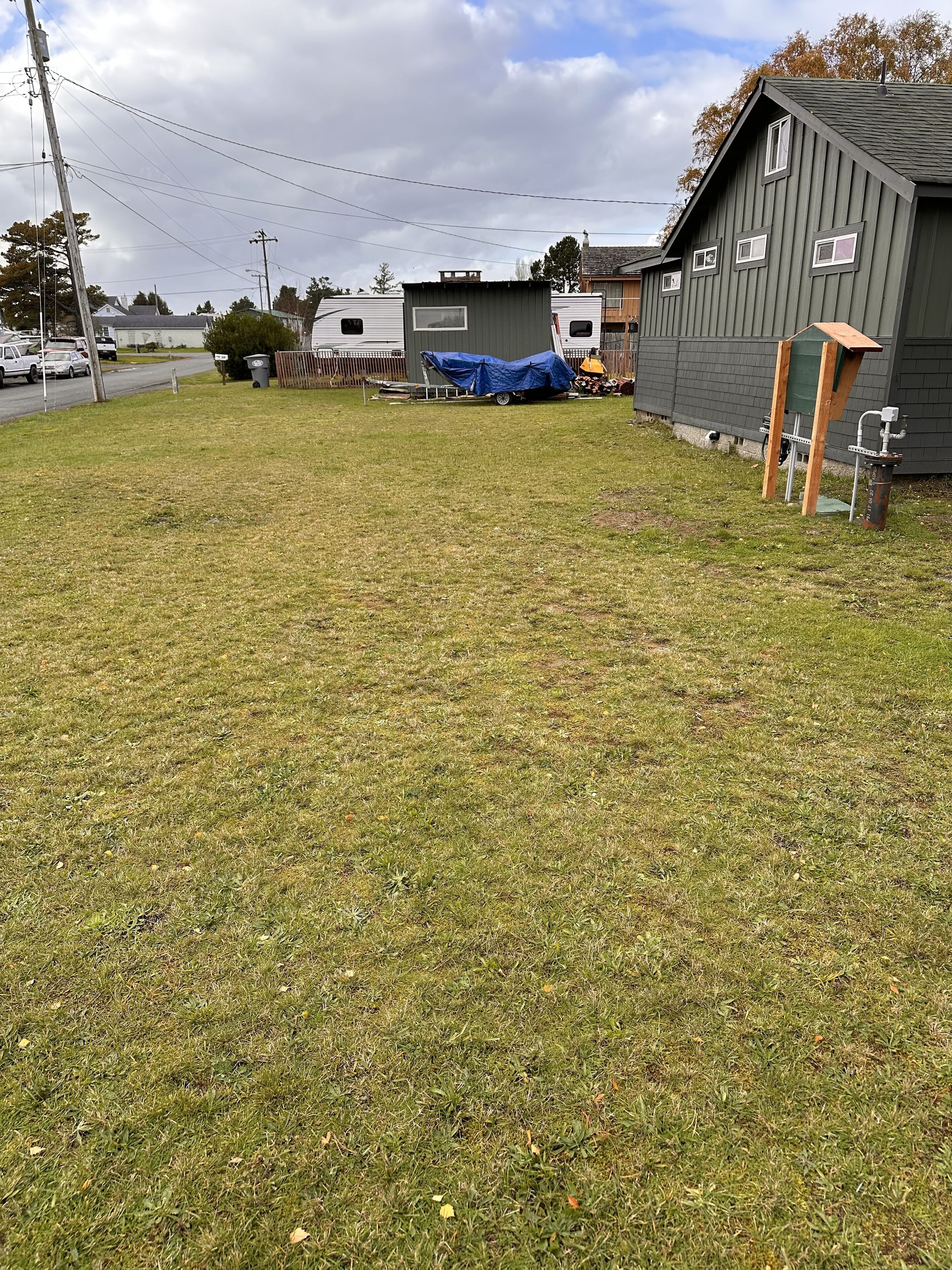 Une zone herbeuse avec un petit abri de jardin et une remorque en arrière-plan.