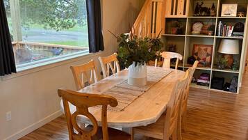 A dining area with a wooden table and chairs, a chandelier, and a bookshelf with various items.