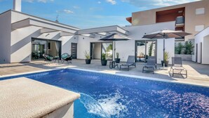 A modern outdoor pool area with a clear blue pool, lounge chairs, and umbrellas.