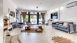 A modern living room with a sofa, a dining area, and a TV mounted on the wall.