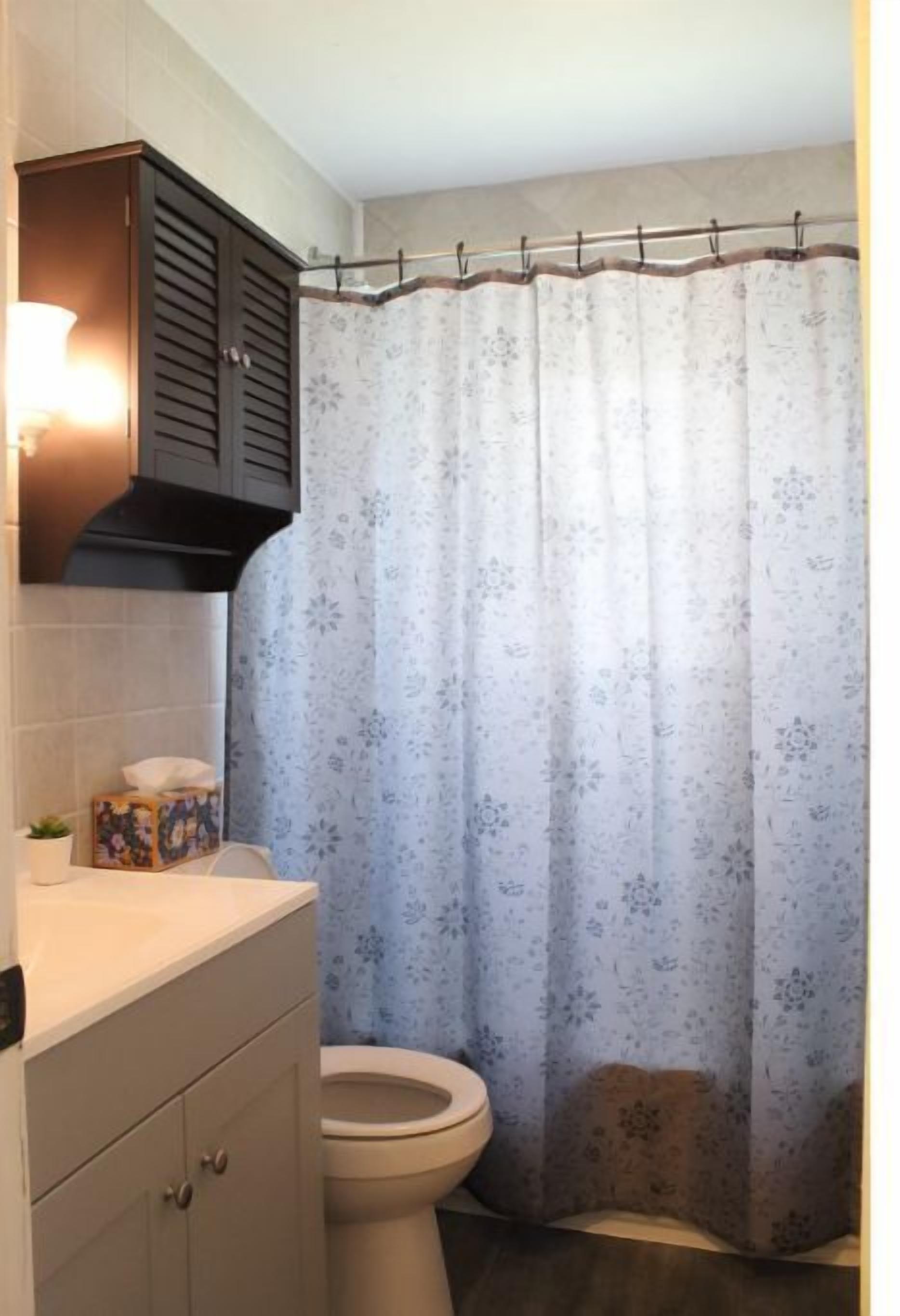A bathroom with a toilet, a cabinet with a towel dispenser, and a shower curtain with a floral pattern.