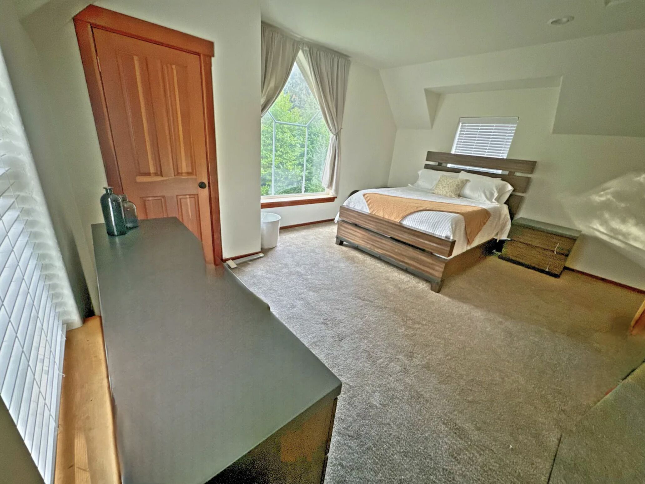 A bedroom with a wooden bed, a bedside table, a window with curtains, and a door.