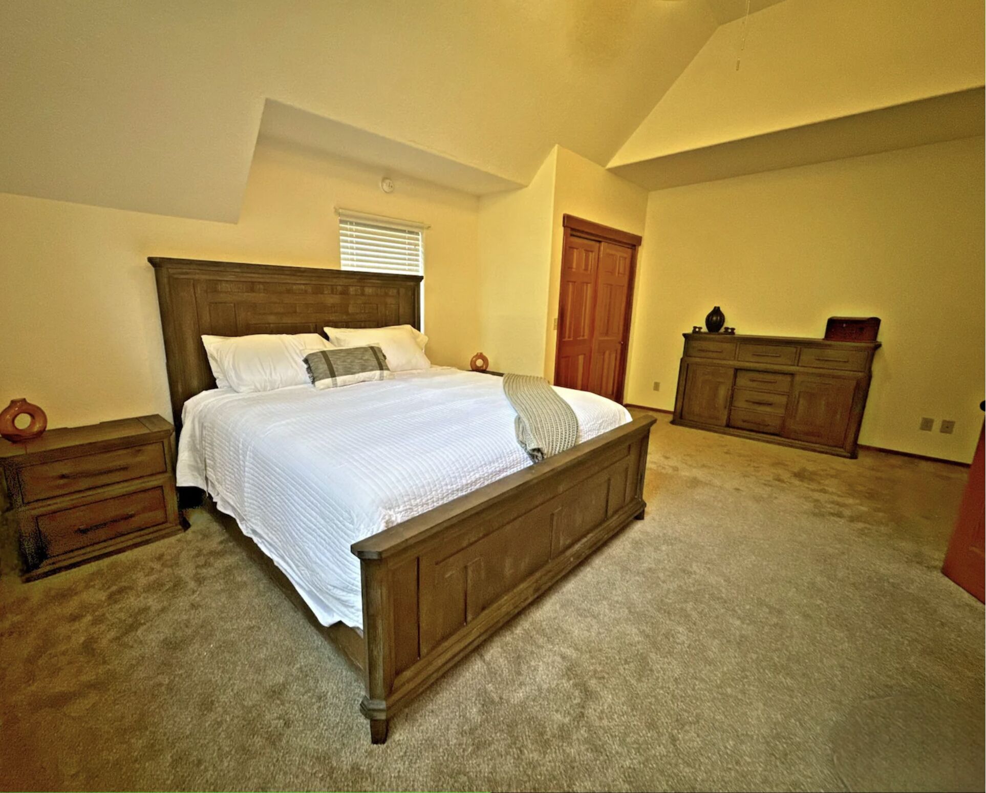 A bedroom with a large bed, wooden headboard, a dresser, and a closet.