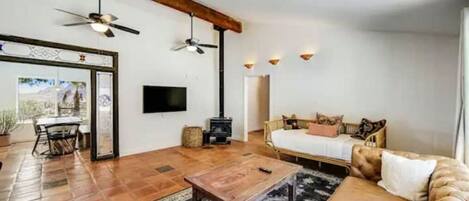 Ein gemütliches Wohnzimmer mit einer Couch, einem Couchtisch und einem Kamin. Ein Fernseher ist an der Wand montiert und ein Deckenventilator vorhanden.