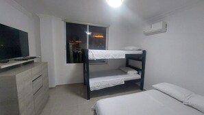 Ein Zimmer mit Etagenbetten, einem Fernseher auf einer Kommode und einem Fenster mit Blick auf die beleuchtete Stadt.