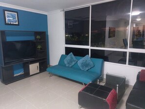 A living room with a blue sofa, a black entertainment unit, and a large window. - Edificio los rosales  (Santa Marta)