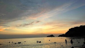 Eine Strandansicht mit badenden Personen und einem Sonnenuntergang im Hintergrund.