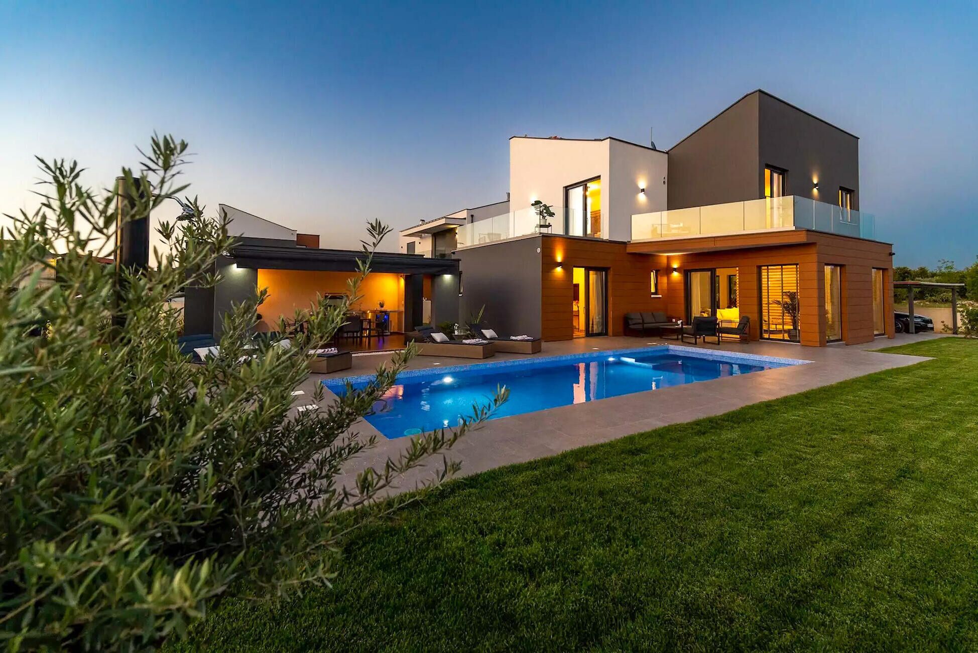 Ein modernes, zweistöckiges Haus mit Schwimmbad, Gartenmöbeln und einem gepflegten Rasen.
