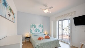 A bedroom with a bed, a ceiling fan, a TV, and a balcony door.