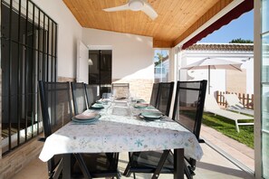 Un espace de restauration en plein air avec une table dressée pour quatre personnes, entourée de chaises, et une vue sur le jardin arrière.