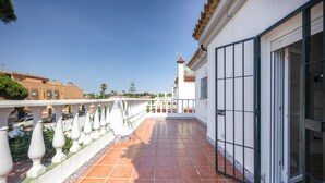 A balcony with a tiled floor, white balustrade, and a view of a building with a red roof.