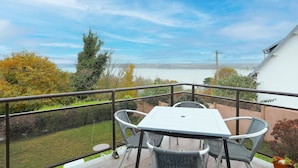 A balcony with a table and chairs, overlooking a garden and a distant view. - Villa 'Bellevue Rue De La Petite Corniche' with Sea View, Private Terrace and Wi-Fi (perros guirec)