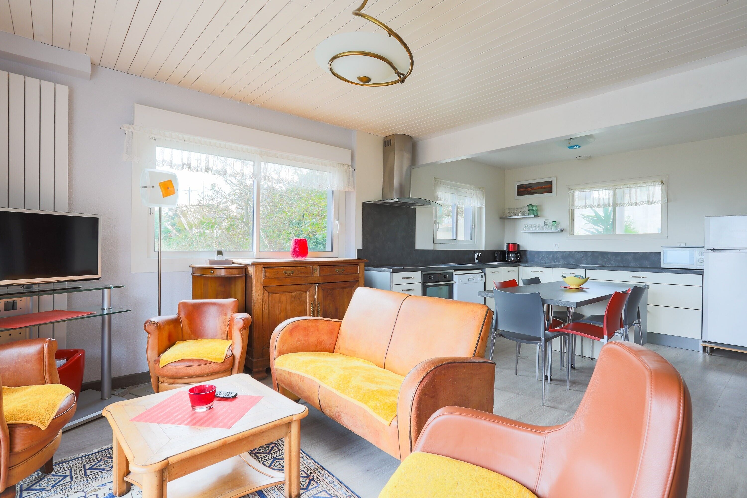 A modern kitchen with a dining area, a TV, and leather chairs.