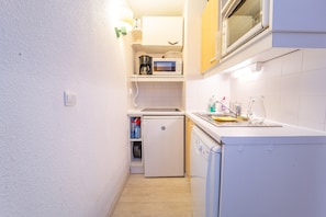 Uma cozinha compacta com micro-ondas, cafeteira e máquina de lavar louça.