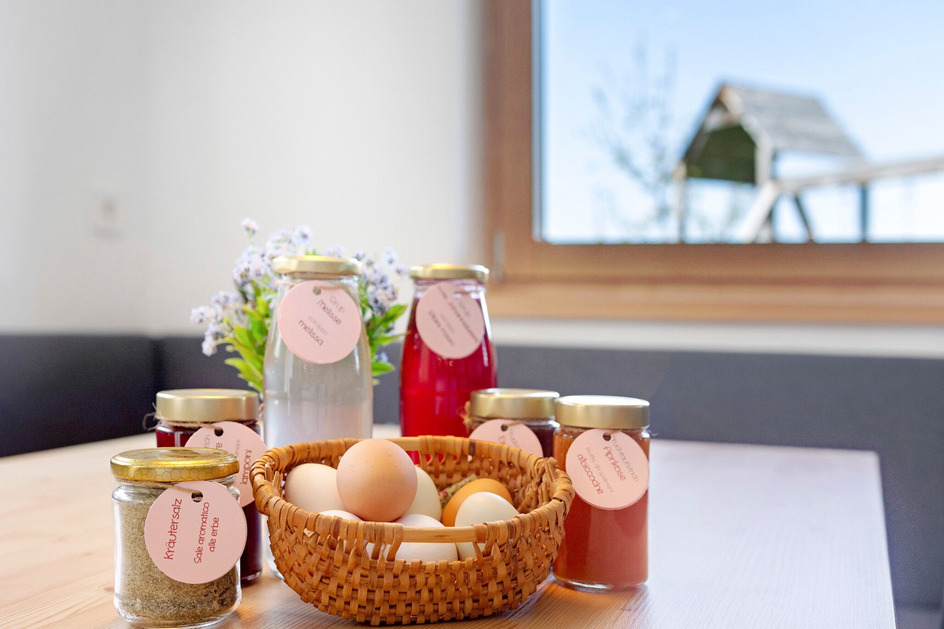Ein Tisch mit Gläsern voller Honig und Eiern, ein Eierkorb und Blick aus dem Fenster.
