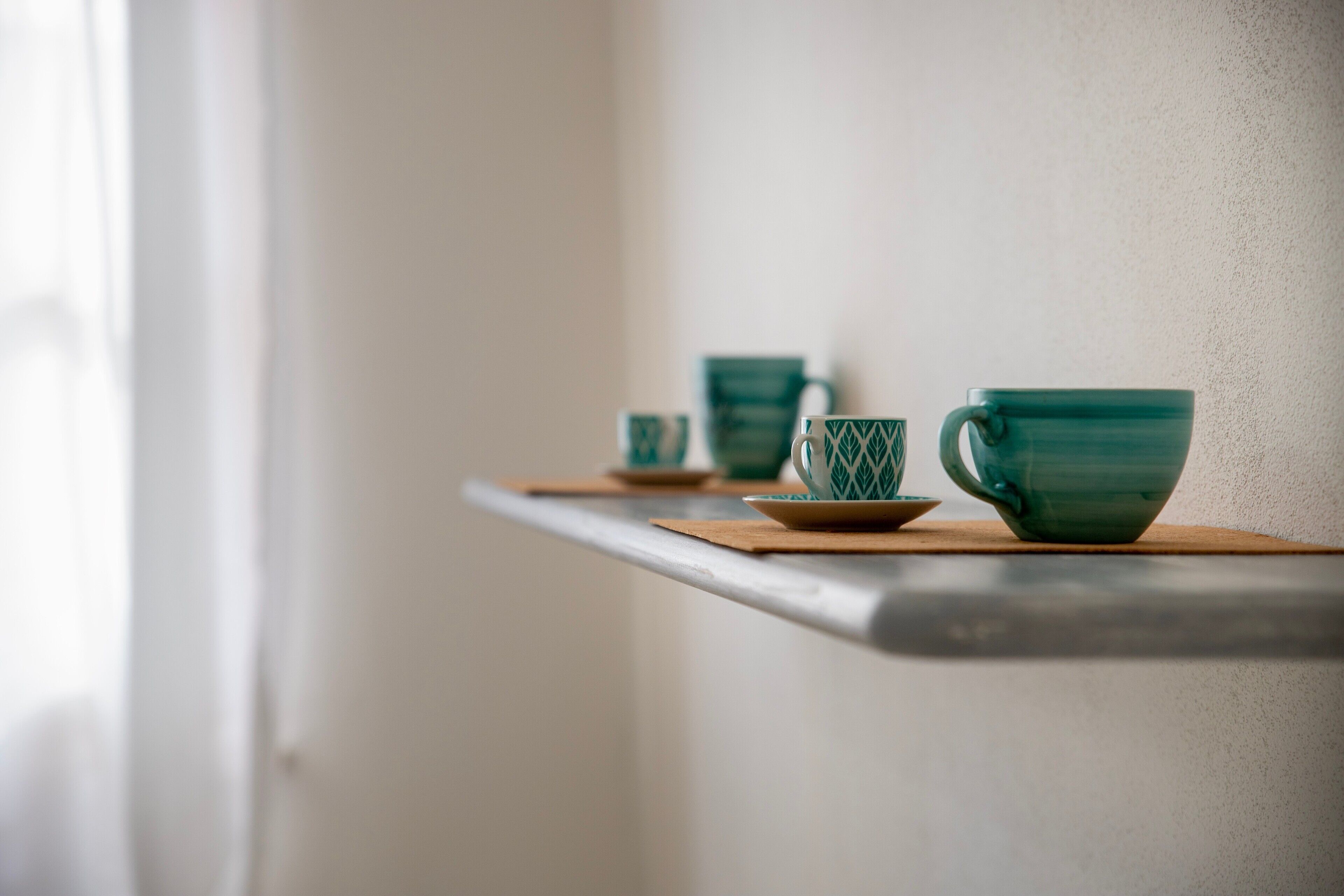 A shelf with three teal ceramic cups and saucers.