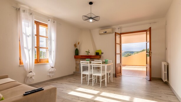 A room with a sofa, a dining table with chairs, a ceiling light fixture, and a view through an open door.