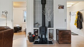 Un salon avec un poêle en bois noir, un canapé en cuir marron, un meuble en bois et une fenêtre donnant sur une maison.