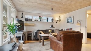 Un salon chaleureux avec un plafond en bois, un canapé en cuir marron, une table basse en bois et un téléviseur posé sur un meuble.