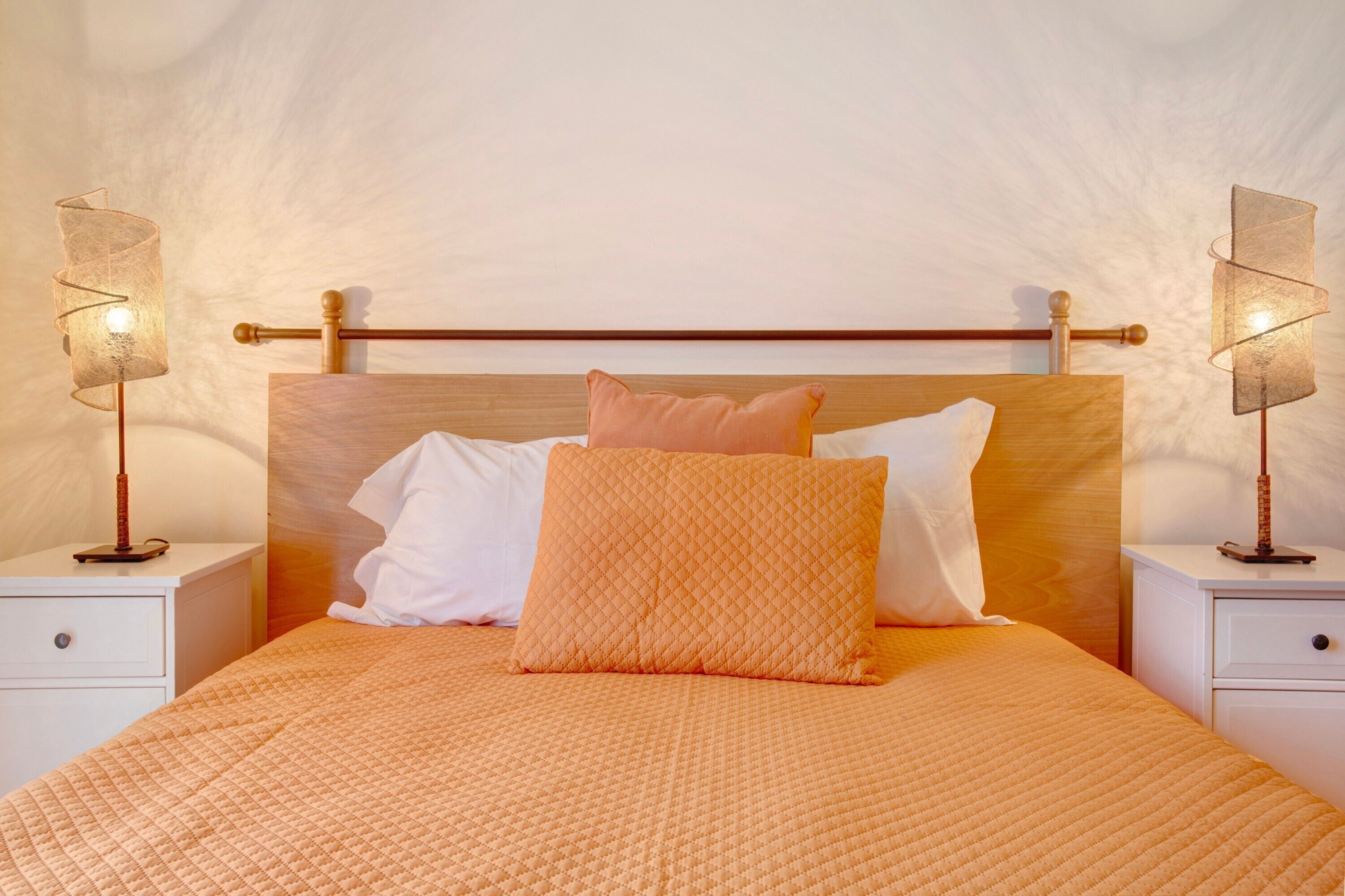 Een bed met een houten hoofdbord, twee nachtkastjes met lampen, en een witte muur.