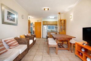 Una sala de estar con sofá, una mesa de comedor de madera, televisión y cocina al fondo.