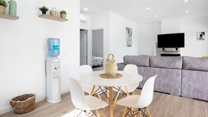 Una sala de estar moderna con un sofá gris, un televisor de pantalla plana y un comedor con una mesa redonda y sillas blancas.