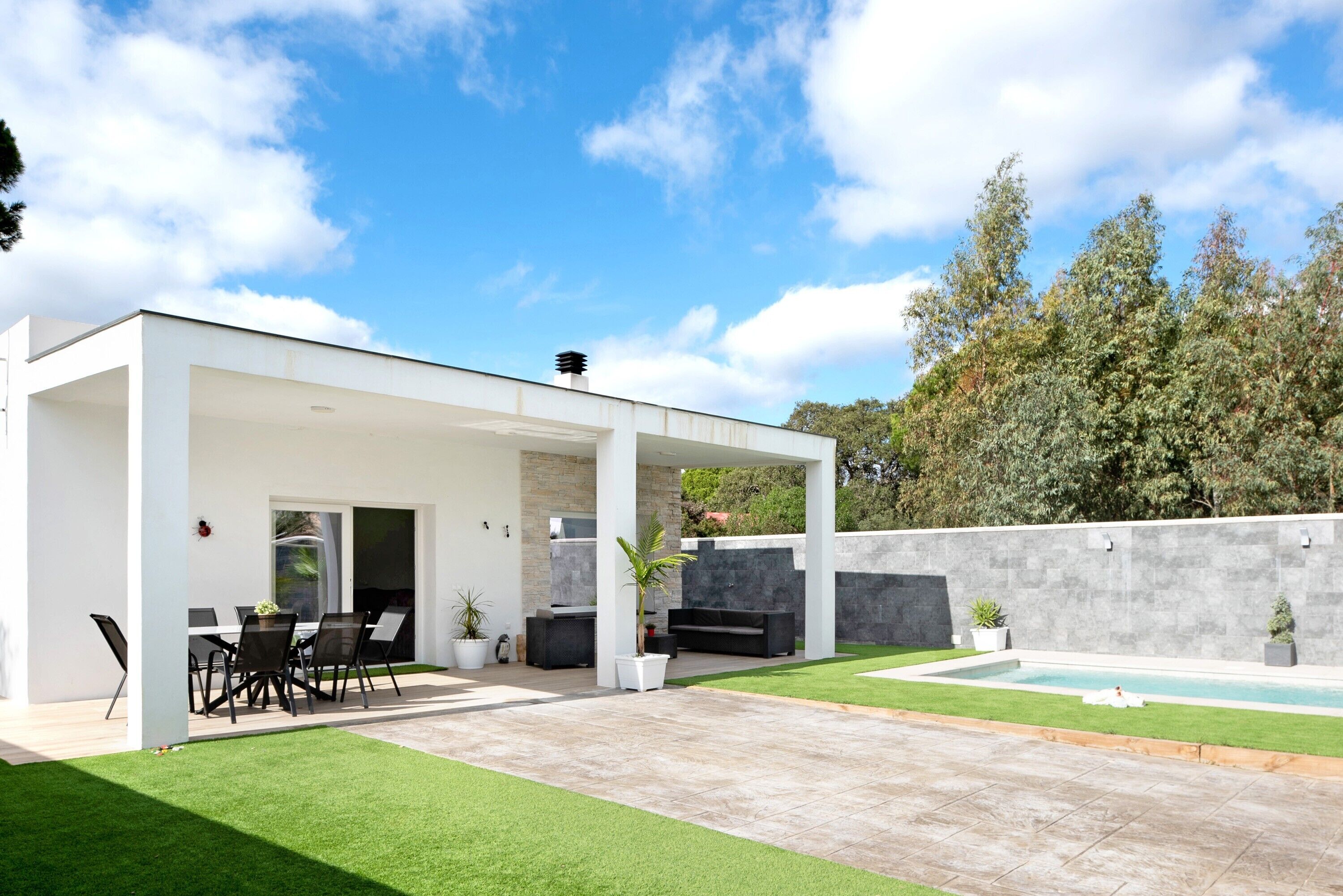 A modern outdoor patio with a pool, seating area, and a covered section.