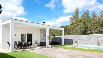 A modern outdoor patio with a pool, seating area, and a covered section.