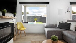 Una sala de estar moderna con chimenea, un sofá, un sillón amarillo y una ventana con vistas a un patio trasero.