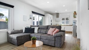 Una sala de estar moderna con un sofá seccional gris, una mesa de centro redonda de madera y una cocina al fondo.
