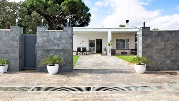 Una casa moderna con fachada de piedra, un árbol grande y un camino pavimentado que conduce a un patio.