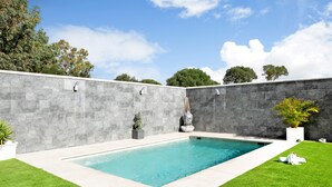Una piscina rectangular con un muro de piedra y césped a ambos lados.