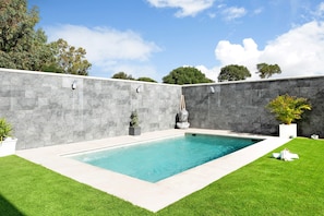 A rectangular swimming pool with a stone wall and grass on either side.
