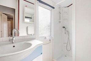 A bathroom with a sink, mirror, shower, and window. - Mobilhome Puget-sur-argens with Shared Pool, Wi-Fi and Air Conditioning (Puget-sur-Argens)