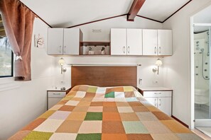 A bedroom with a wooden headboard, white cabinets, a quilt, and a shower. - Mobilhome Puget-sur-argens with Shared Pool, Wi-Fi and Air Conditioning (Puget-sur-Argens)