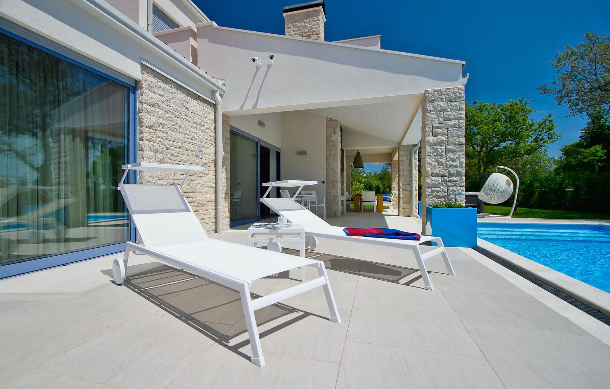 A modern outdoor pool area with white lounge chairs and a covered seating area.