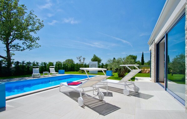 A modern outdoor pool area with a clear blue pool, white sun loungers, and a glass-enclosed patio. - Nice home in Porec with sauna (Porec)