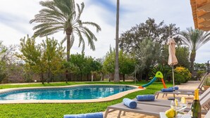 Una piscina con tobogán, sillas de descanso y una mesa con una botella y vasos.