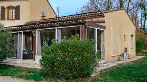 Ein Haus mit überdachter Terrasse, einem kleinen Garten und einem Fenster mit Blick auf die Umgebung.