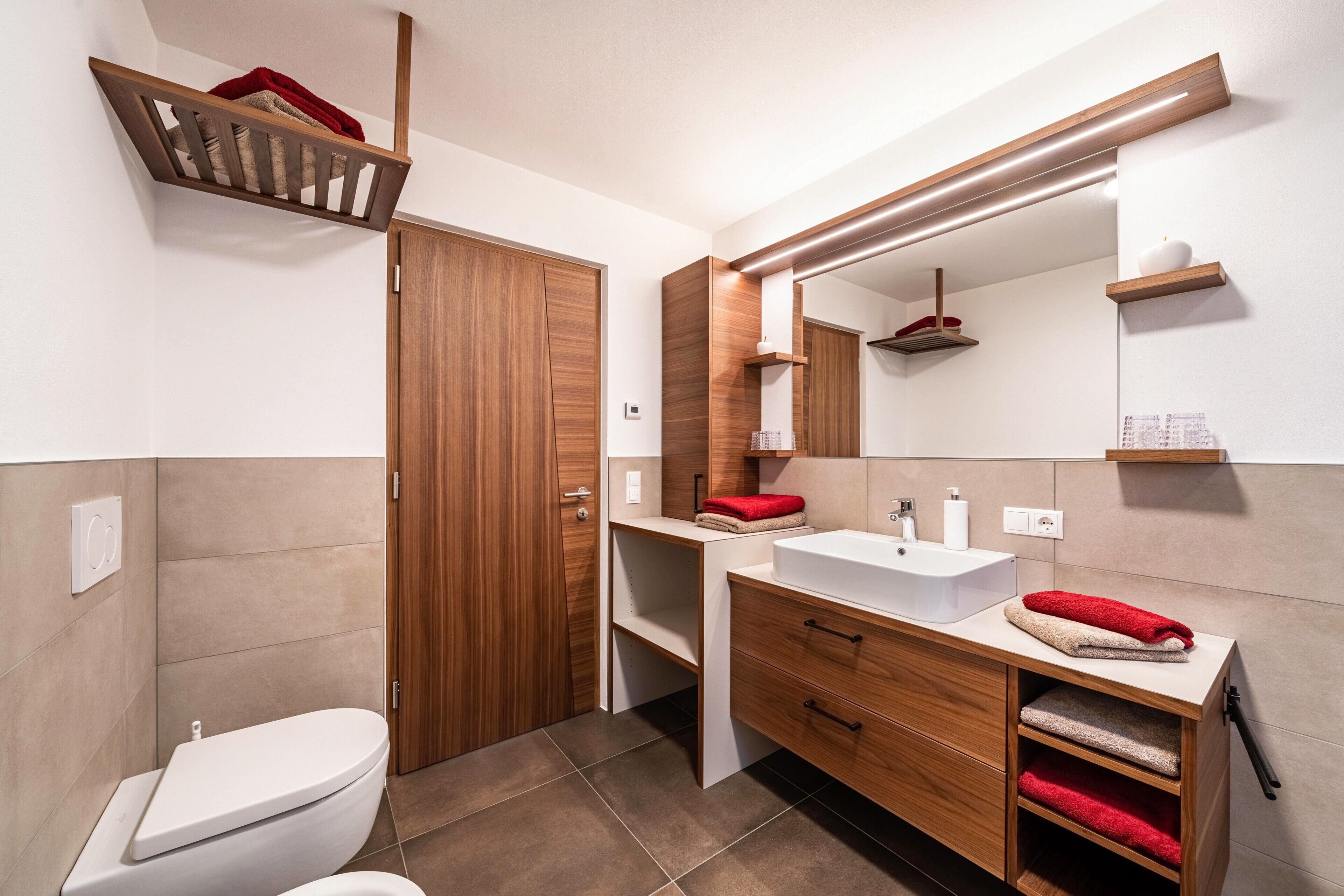 A modern bathroom with a toilet, vanity, mirror, and wooden shelving.
