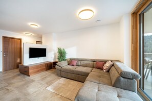 A modern living room with a sectional sofa, a flat-screen TV, a wooden cabinet, and a large window. - Apartment 'Klara' with Mountain View, Private Terrace and Wi-Fi (Mölten)