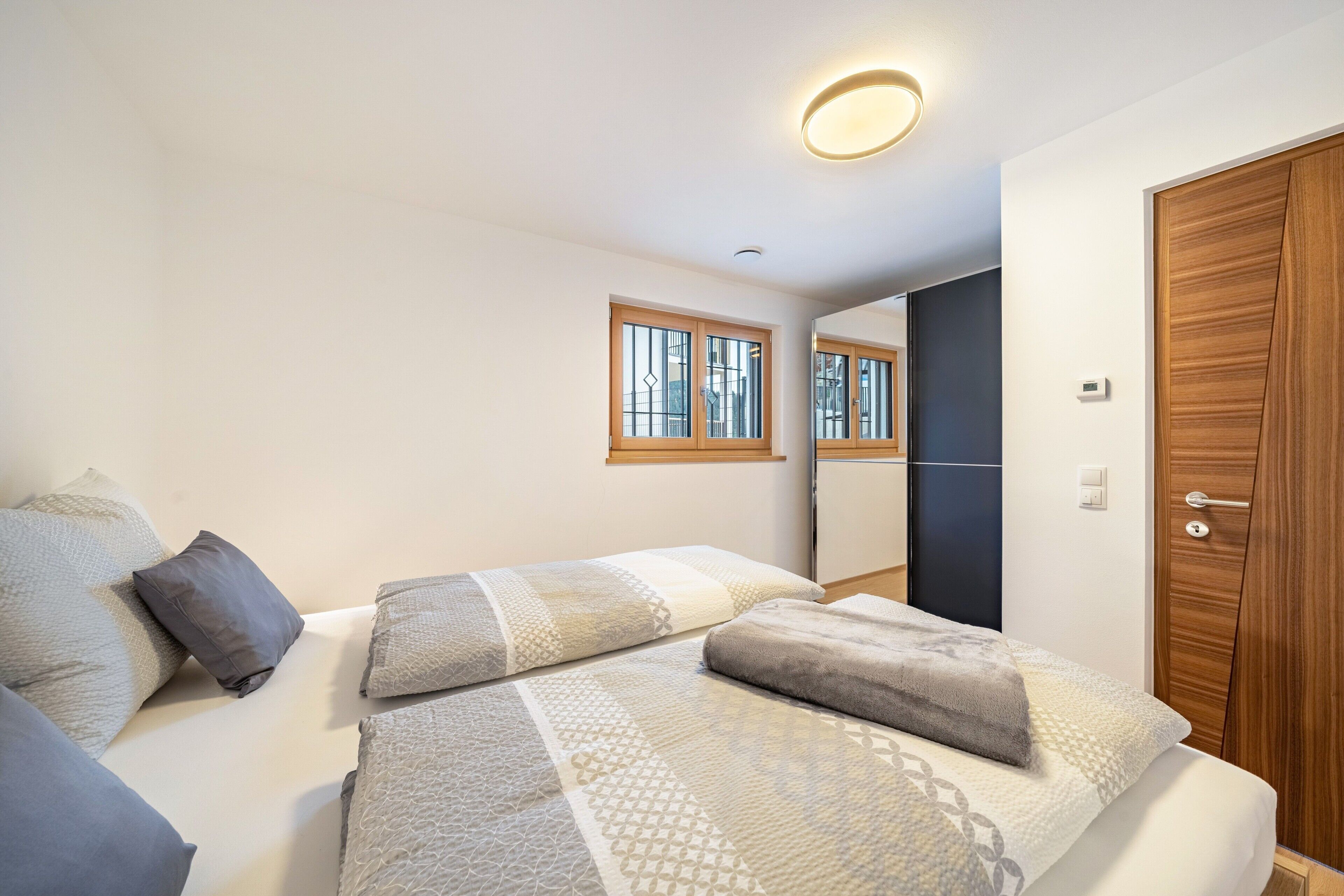 Un dormitorio con cama, almohadas, ventana, puerta y lámpara en el techo.